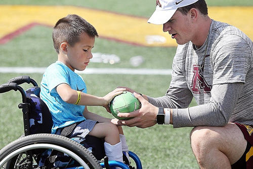 A child grips a football player held by a Golden Gopher athlete at the HopeDay Festival.