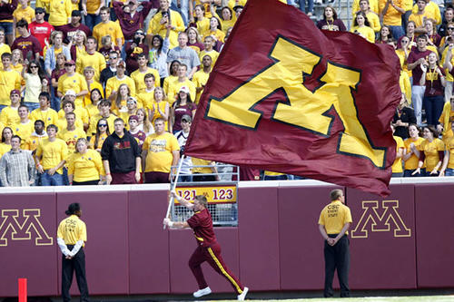 A male cheerleader carries and M flag around the perimeter of TCF Bank Stadium.