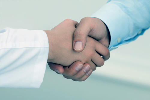 A pair of hands shake hands. One hand is in white coat.