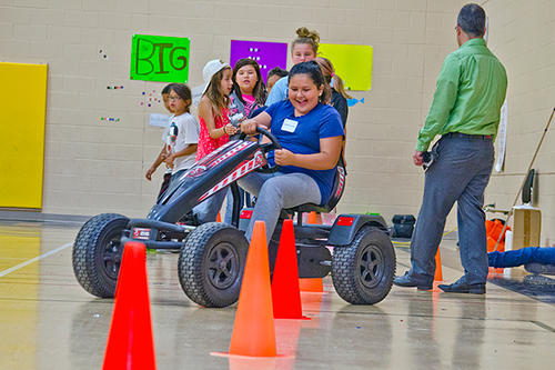 A student maneuvers a pedal cart through orange cones.