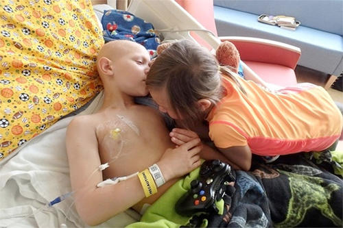 A young girl hugs her brother on a hospital bed