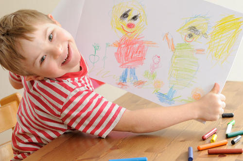 A young student holding a crayon drawing. 
