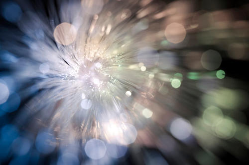 Abstract of light-reflecting fibers radiating from a central area like a flower, with unfocused droplets of blue, green, and pink.