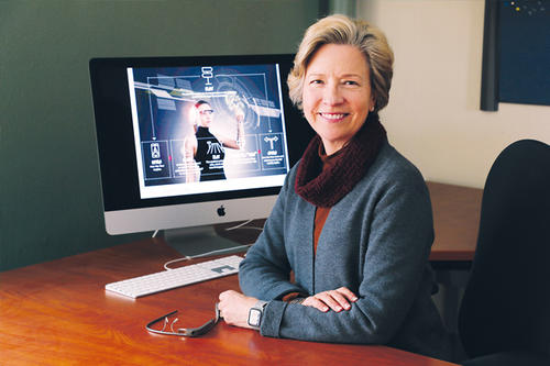 Ann Hill Duin, short hair, sits with a computer screen behind her. 