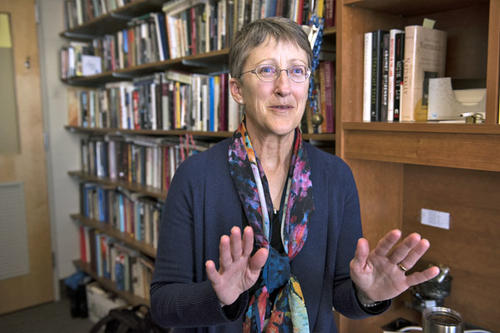 Barbara Welke, in short hair, wire-rims and a sweater, stands in front of a bookcase.