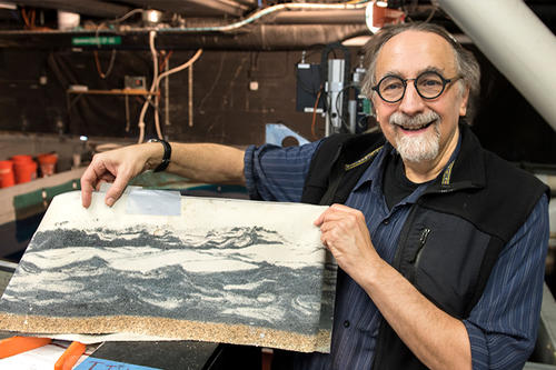 Chris Paola, balding, goatee, large glasses, holds a topographical map.