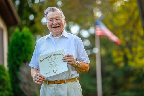 Dan Cylkowski holds up his diploma on the front lawn of his home. 