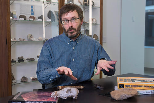 David L. Fox, in glasses and beard, before a display case of rocks.