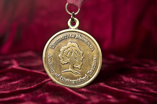 Gold medallion with embossed tree and words &quot;Academy of Distinguished Teachers&quot; against a maroon background.