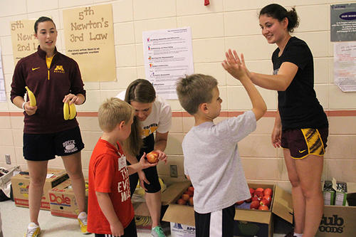Gopher student-athletes hand out fruit to and high-five students from an elementary school.