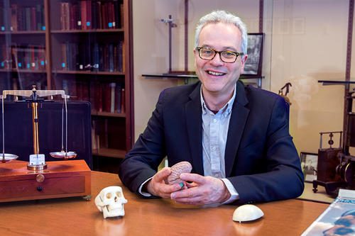 Jonathan Gewirtz, with white hair and glasses, a tiny plastic skull, and a balance scale, smiles from his office desk chair.