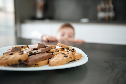Little boy standing in the kitchen trying reach for chocolate chip cookies.