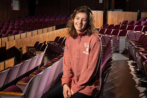 Maizie Deihl, in Sienna clay Bulldog sweatshirt, poses among the seats of an auditorium.