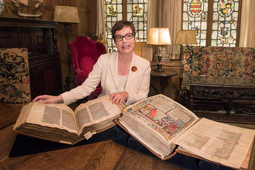 Mary Franklin-Brown, with dark hair and big glasses, sits with an open Medieval text.