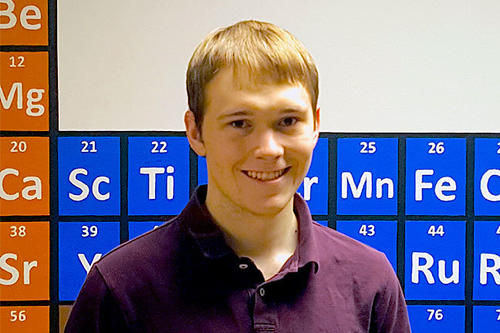Merrick Pierson Smela, blond with a grin, poses next to the 3-d periodic table display in Kolthoff Hall.