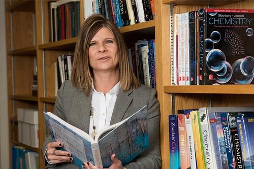 Michelle D. Driessen holds a book next to a bookshelf.