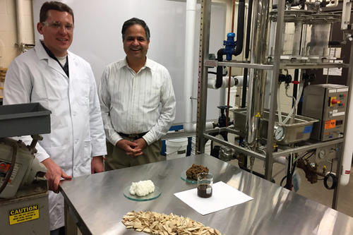 Researcher Lucas Stolp and Professor Shri Ramaswamy next to a thin film evaporator and displaying (clockwise) white pulp, craft pulp, black liquor (in the beaker), and woodchips.