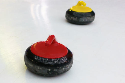 Two curling stones, one red/maroon and the other gold, on a sheet of ice