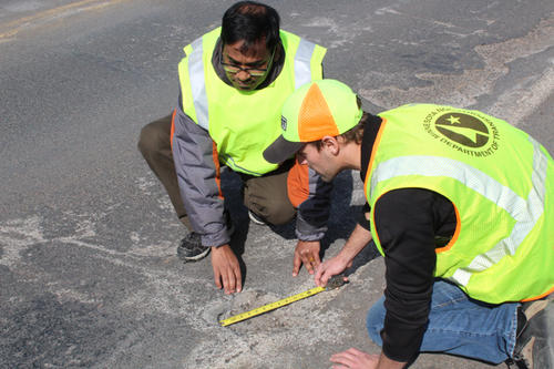 Two people measuring a pothole. 