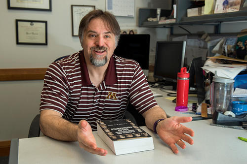 Victor Barocas, with dark hair and goatee, in a striped polo, at his desk.