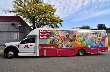 The colorfully painted mobile health initiative vehicle, with a white truck cab followed by a mural of community faces painted on the trailer, is parked on the side of a street.
