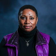 Rhonda Franklin wearing bright purple winter vest and black clothes in front of dark blue cloudy background