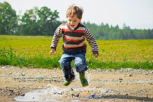 A young boy splashes in a puddle in a rural landscape.
