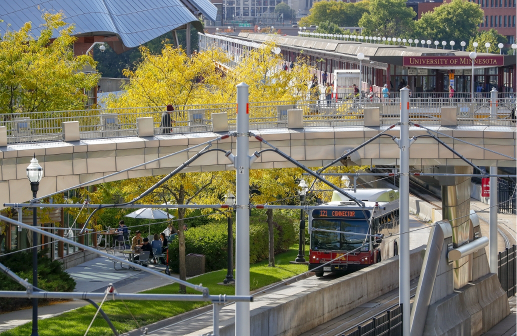 view of the Washington Ave transit center with view of pedestrian bridge, Washington St bridge, hybrid-power bus, light rail tracks, and Weisman Museum in background