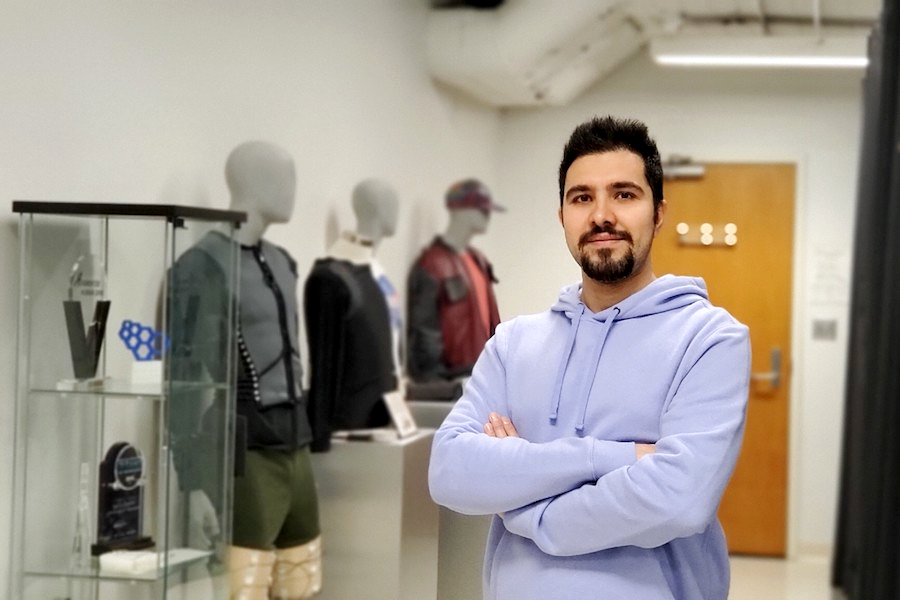 Alireza Golgouneh stands with folded arms before three manikins in variously colored jackets.